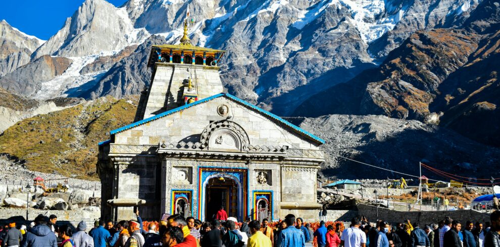 Crowd gathers at Kedarnath Temple with Himalayas backdrop, showcasing religious significance and stunning landscape.